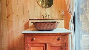 A wooden bathroom with a round mirror, a wooden cabinet with drawers, and a basin. - TATA River Cabins- group getaway (Salida)