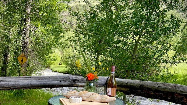 A picnic table with two wooden chairs, a bottle, a jar of jam, and a loaf of bread on a glass table. - TATA River Cabins- group getaway (Salida)
