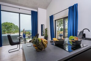 Enjoy a kitchen with a large window offering a view of the outdoors, featuring a black countertop, induction cooktop, and a bowl of fresh fruits.