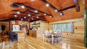 Interior de una cabaña de madera con cocina, comedor y ventanas amplias.