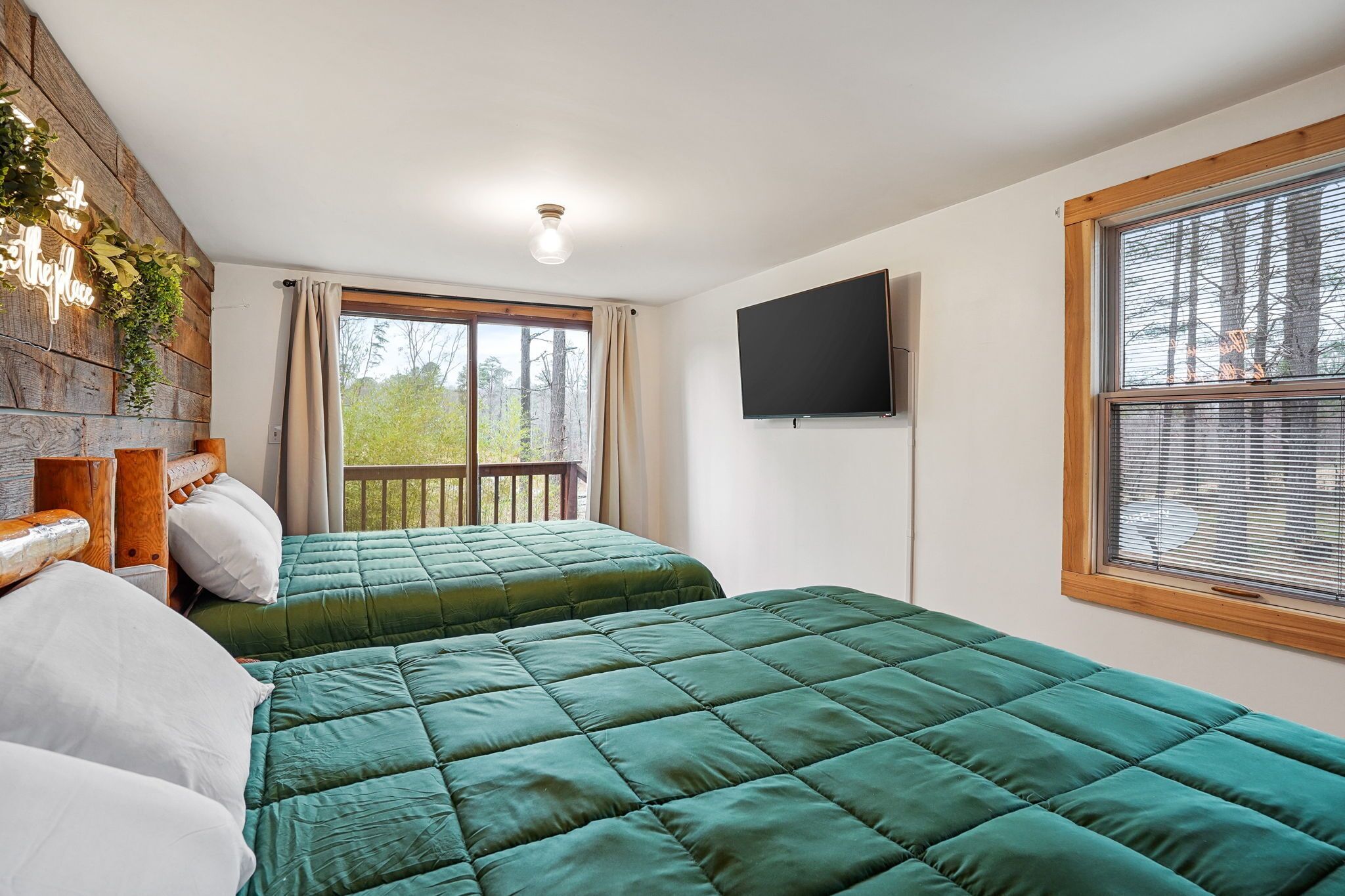 Une chambre avec deux lits, une télévision, une fenêtre avec des stores et un mur en bois orné de plantes.