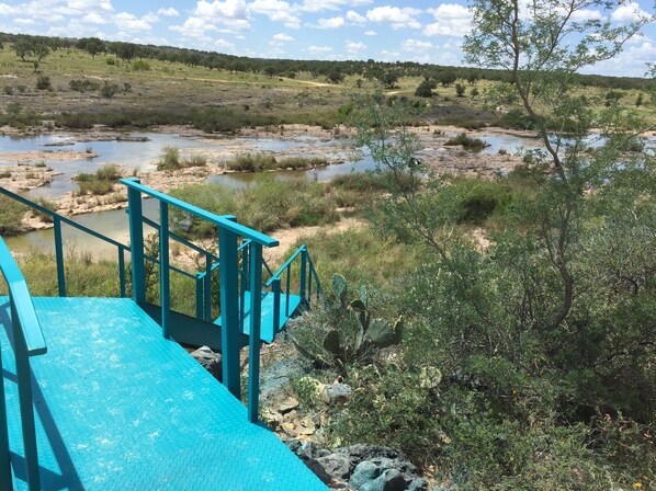 A turquoise staircase leading down to a riverbank with sparse vegetation and distant trees.