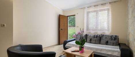 A living room with a sofa, two black chairs, a wooden coffee table, and a window with a curtain.