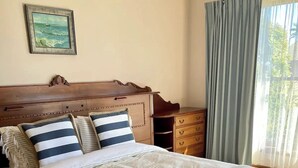 Een net opgemaakt bed met gestreept beddengoed, een houten hoofdbord, een klein nachtkastje en een nachtkastje.