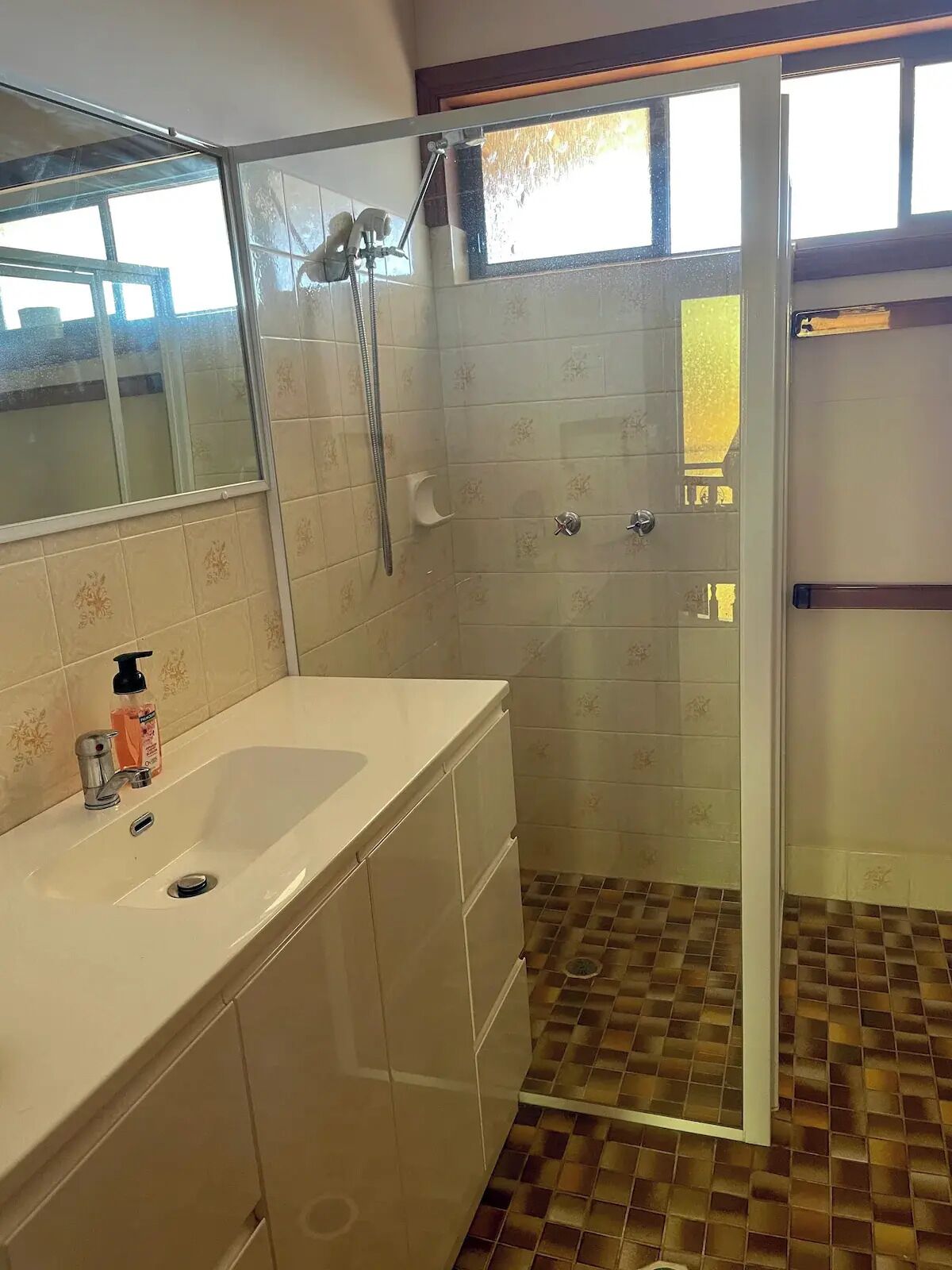 A bathroom with a glass-enclosed shower, a white sink with a soap dispenser, and patterned tiles on the walls and floor.