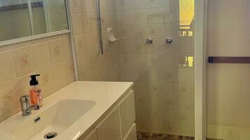 A bathroom with a glass-enclosed shower, a white sink with a soap dispenser, and patterned tiles on the walls and floor.