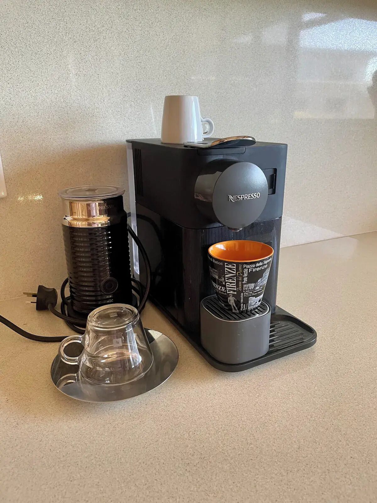 Nespresso-kahvinkeitin, jossa on lasinen vesisäiliö ja mukiteline.