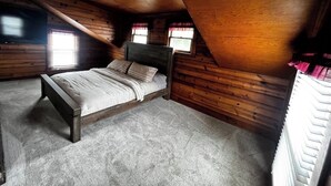 A bedroom with a wooden sloped ceiling, a bed with a grey carpet, and two windows with curtains. - Lake front updated cabin-close to everything!! (Ashtabula)