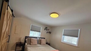 A bedroom with a bed, two bedside tables, a nightstand, a ceiling light, and two windows with blinds. - The Romantic Getaway W/Fireplace-Grill-Fire pit-walkable distance to the Lake! (Pocono Lake)