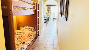 A narrow hallway with a bunk bed on the left and a dining area with chairs and a table on the right.