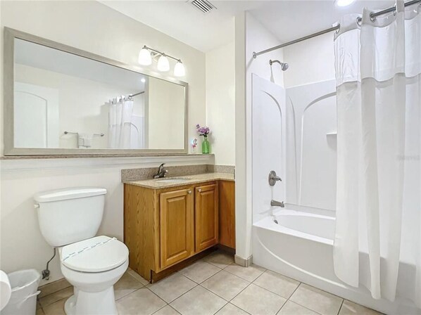 A bathroom with a toilet, wooden cabinets, a sink, a mirror, and a shower with curtains.