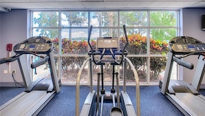 A gym with treadmills and a stationary bike, large windows with a view of trees and plants.