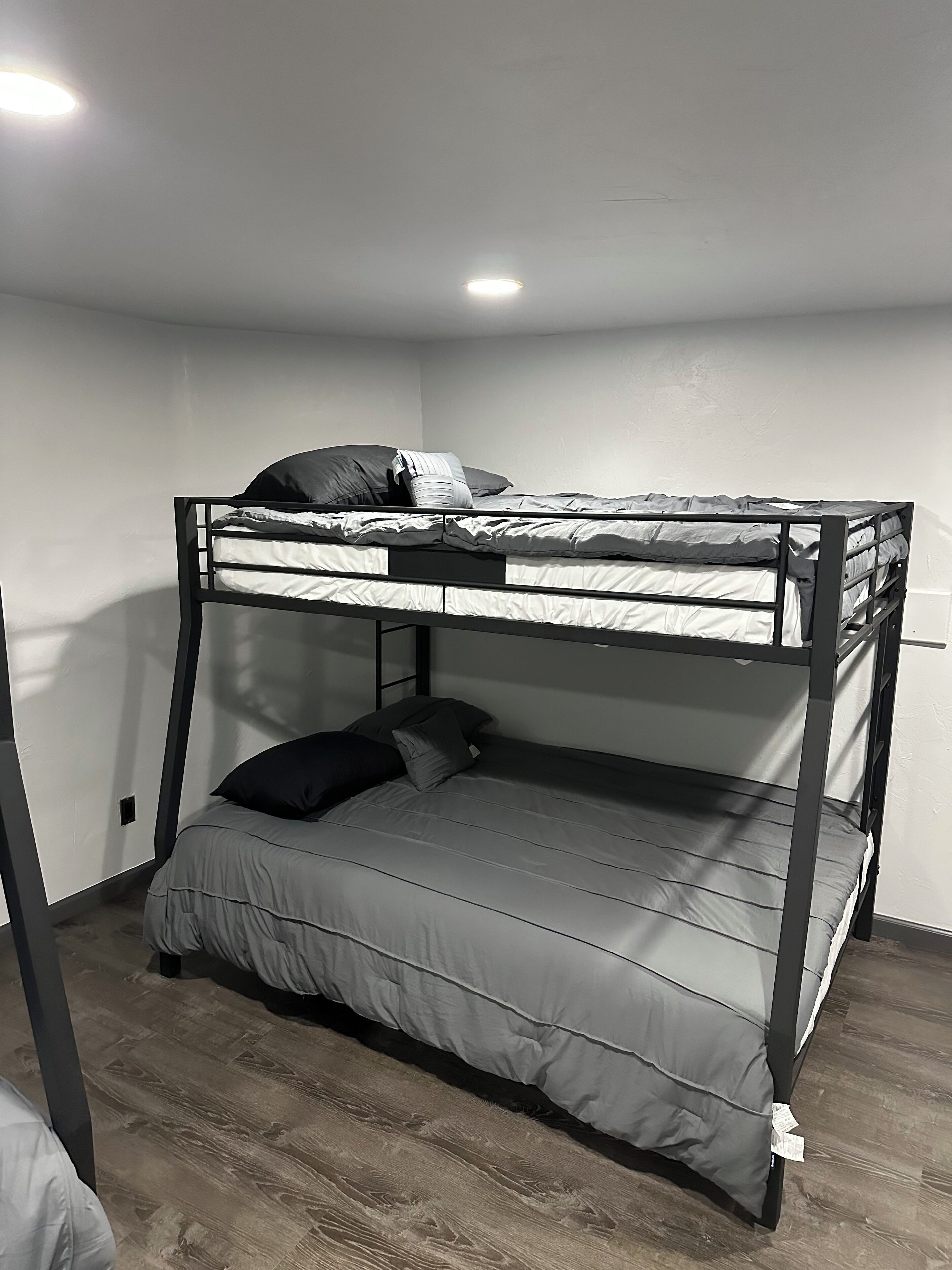 Ein Stockbett mit Matratze und Kissen, ein Holzboden und eine weiße Wand.