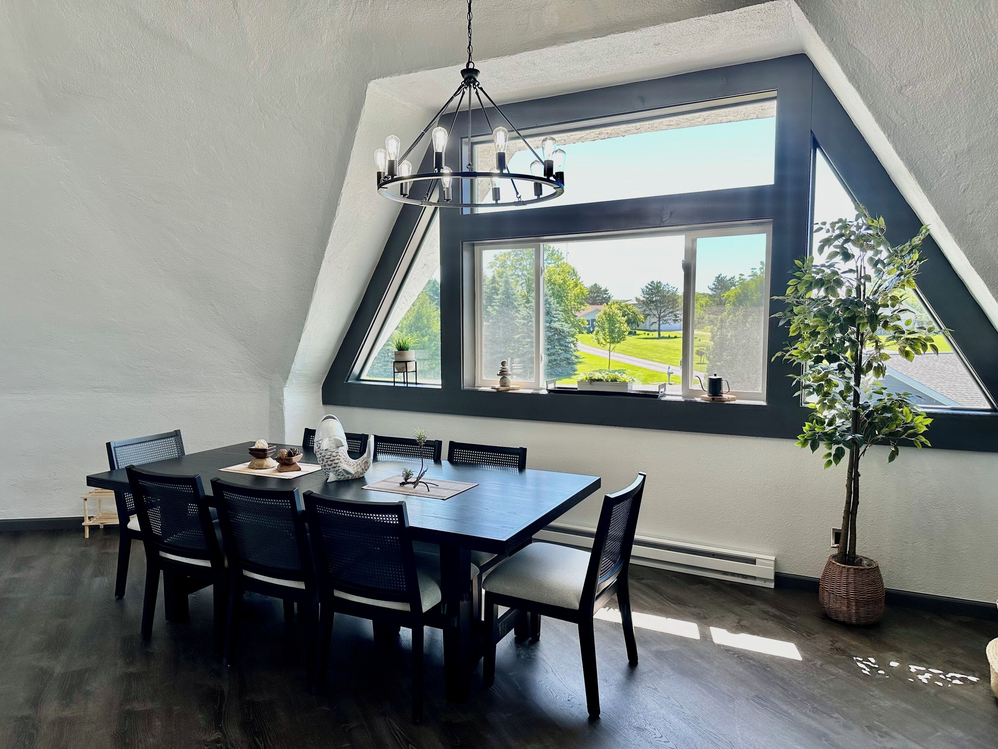 Een eetgedeelte met een tafel en stoelen, een kroonluchter en uitzicht op een groen landschap door grote ramen.
