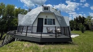 A geodesic dome house with a flat roof, a small entrance, and a balcony with a railing.
