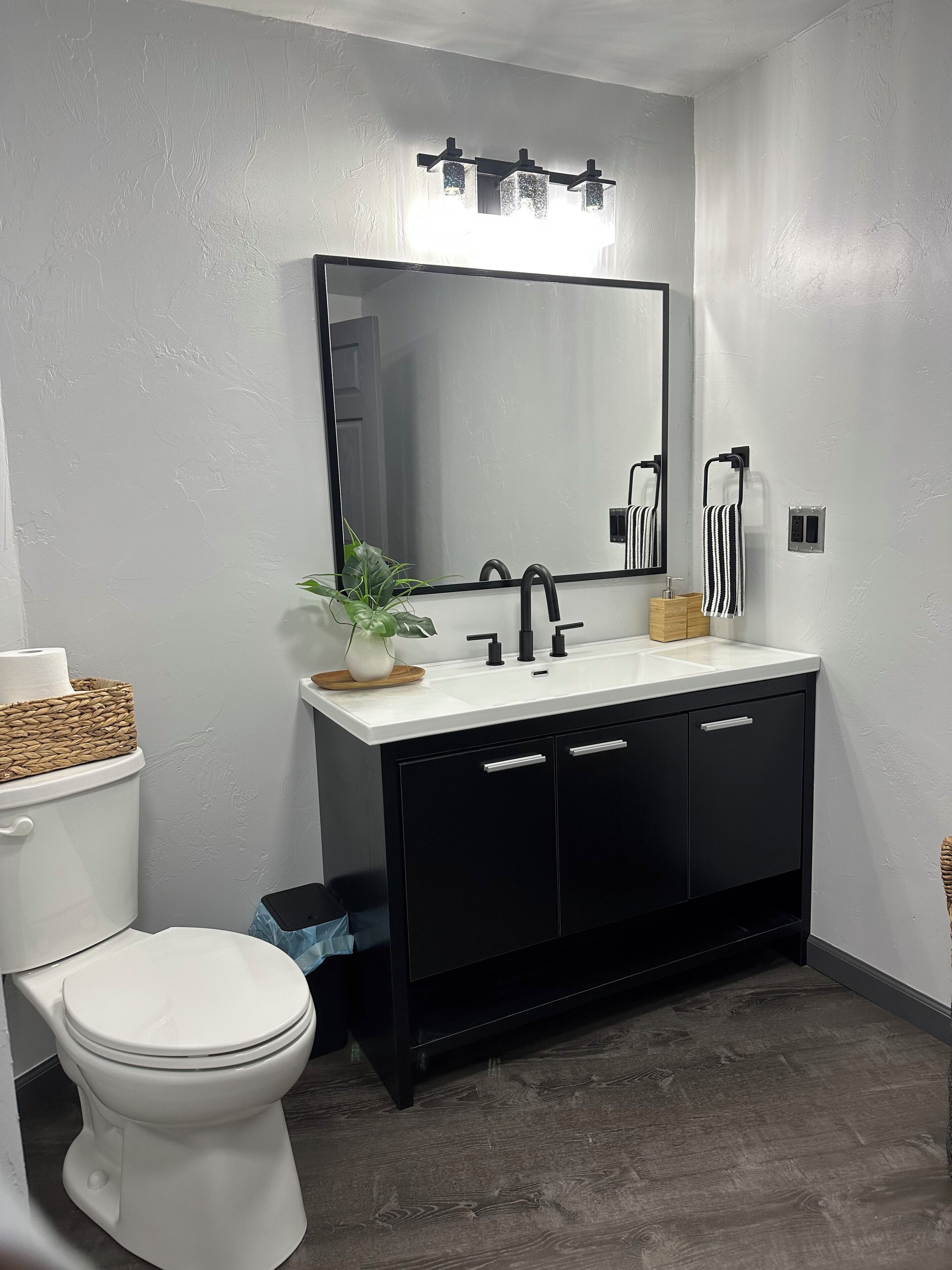 A modern bathroom with a white toilet, black vanity, and a large mirror above the sink.