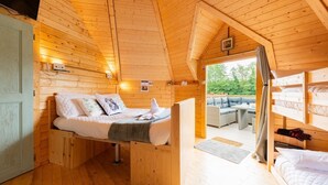 A wooden cabin interior with a bed, a sofa, and a view of the outdoors. - Woods Meadow Glamping (West Malling)