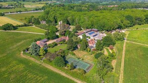 An aerial view of a residential area with houses, a tennis court, and surrounding fields. - Woods Meadow Glamping (West Malling)