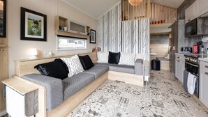 A modern living room with a sofa, a dining area, and a kitchen. - Woods Meadow Glamping (West Malling)