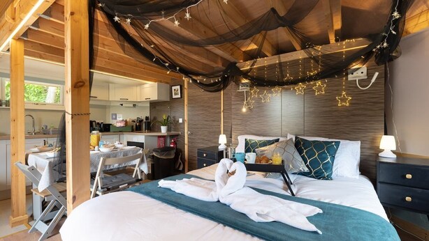 A cozy room with a bed, a desk, and a kitchenette. - Woods Meadow Glamping (West Malling)