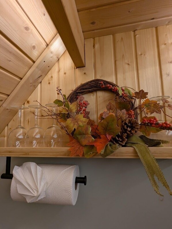 A wooden shelf with clear glass bottles, a decorative wreath, and a roll of toilet paper. - Woods Meadow Glamping (West Malling)