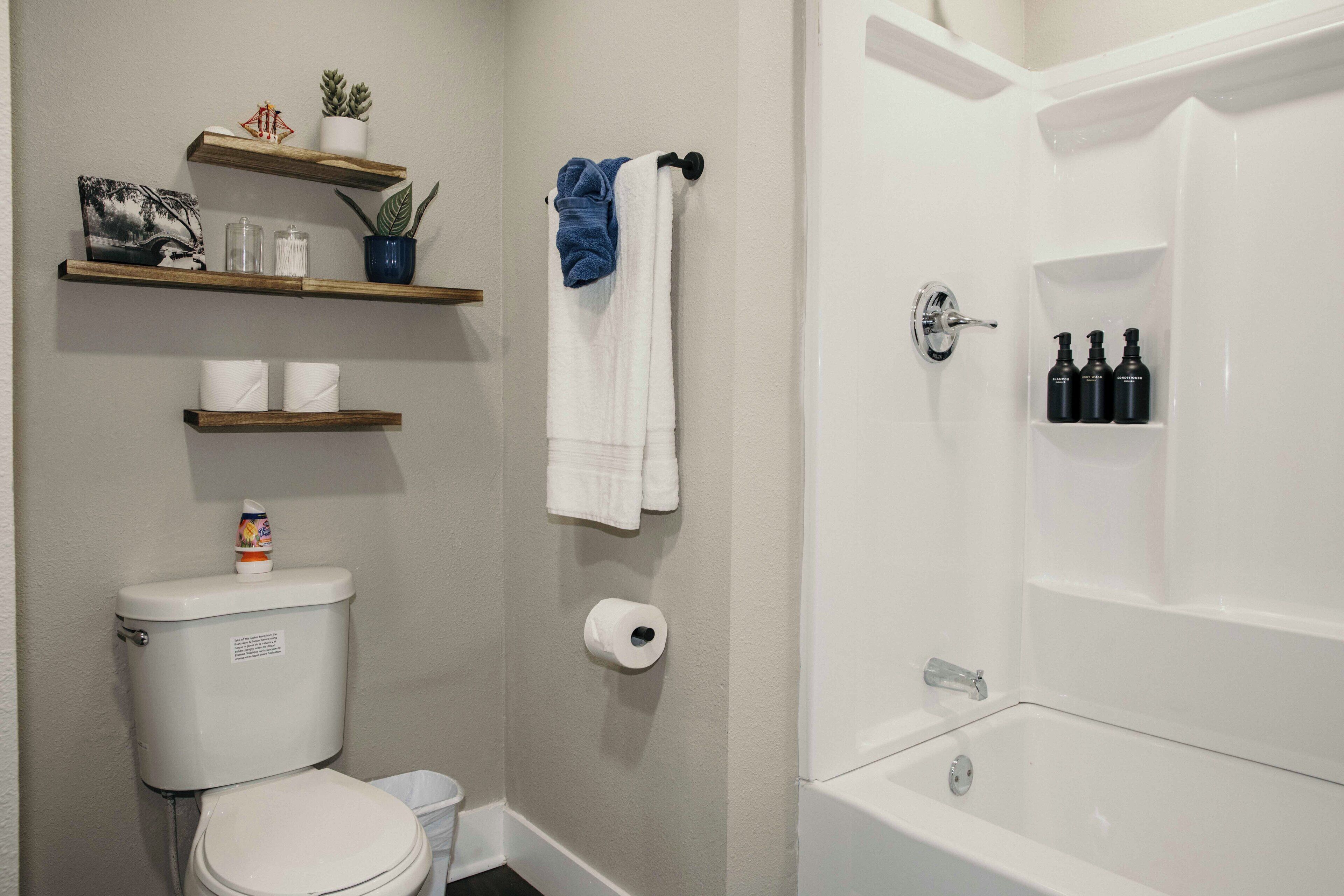 A bathroom with a toilet, a shower, and shelves with toiletries.