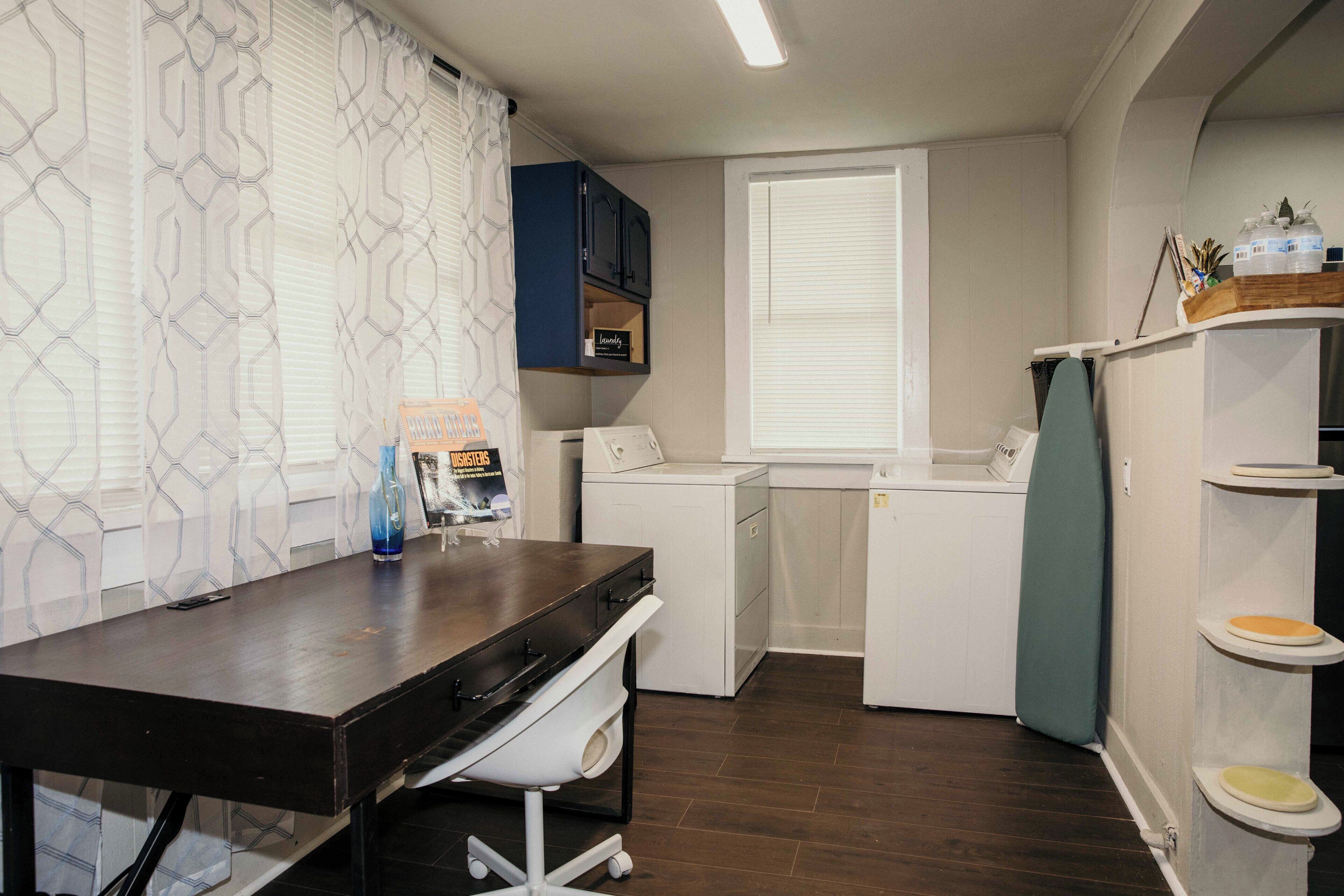 Una cocina compacta con una mesa de madera oscura, una lavadora, una secadora y un estante pequeño con algunos objetos.