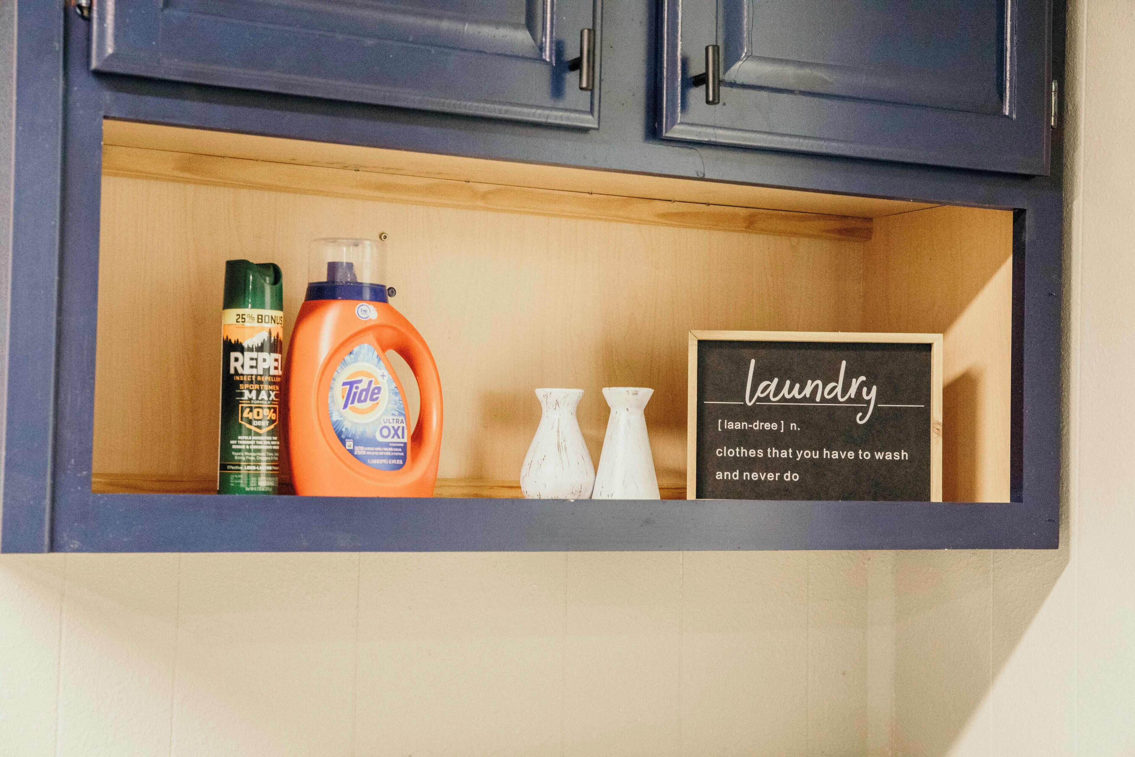 A wooden shelf with Tide detergent, a REPEL can, and a small chalkboard with a laundry note.