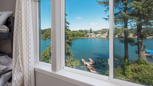 A room with a large window overlooking a lake, surrounded by trees and houses. - Lakefront Townhome with Dock on Devils Lake (Lincoln City)