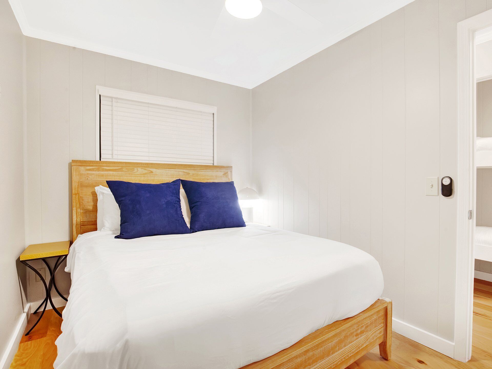 A bedroom with a wooden bed, white bedding, and a small table with a chair.