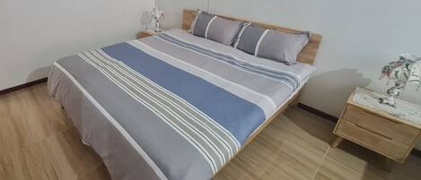 Una cama bien hecha con ropa de cama a rayas, un cabecero de madera y una mesita de noche con un objeto decorativo.