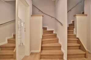Una escalera de madera con barandilla, paredes blancas y piso de color claro.