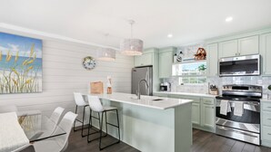 A modern kitchen with a central island, stainless steel appliances, and a view of the sea. - Shoreline Breeze | Steps to the Beach | Beautiful views from 2nd and 3rd balconies (Inlet Beach)