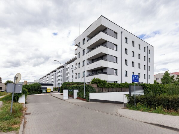 A modern multi-story residential building with balconies, a gated entrance, and a clear sky.