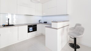 Une cuisine moderne avec des meubles blancs, un four encastré et un tabouret de bar.