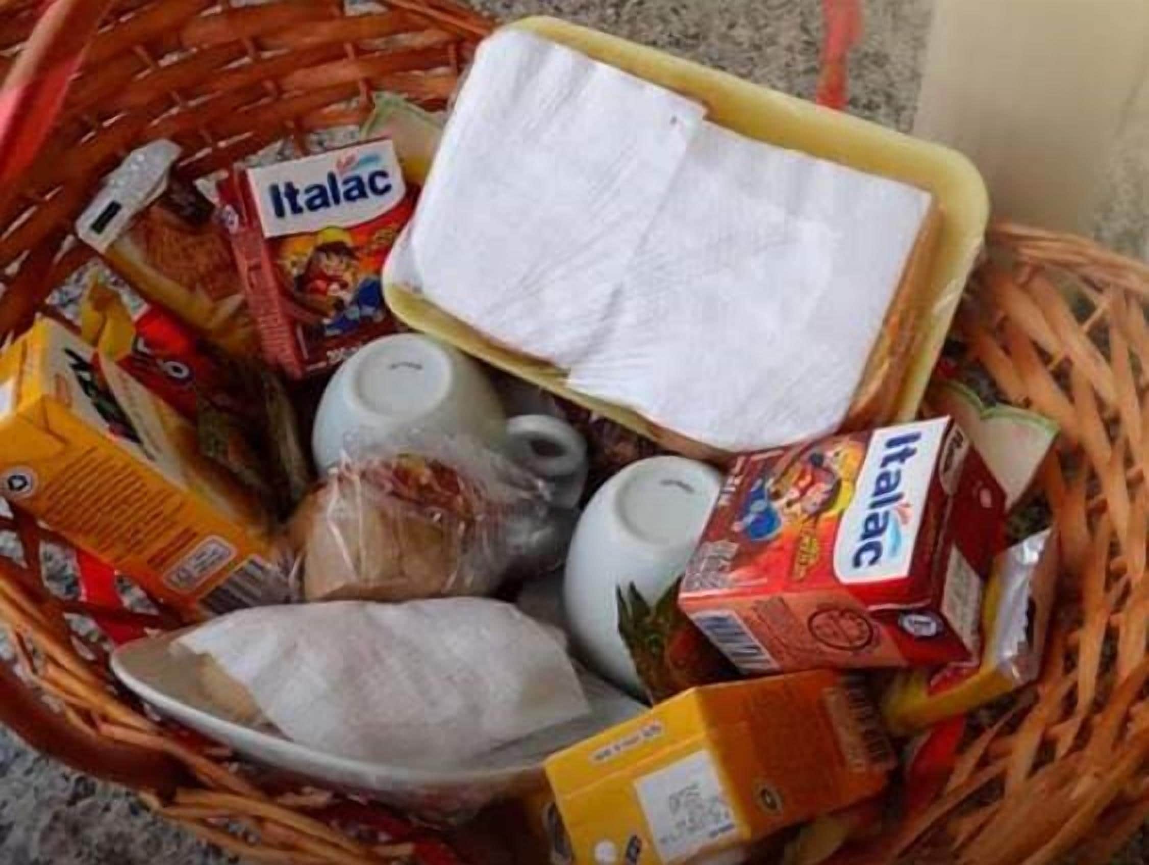 Uma cesta com diversos artigos de mercearia, incluindo caixas de Italac e outros produtos embalados.
