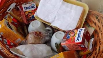 Uma cesta com diversos artigos de mercearia, incluindo caixas de Italac e outros produtos embalados.