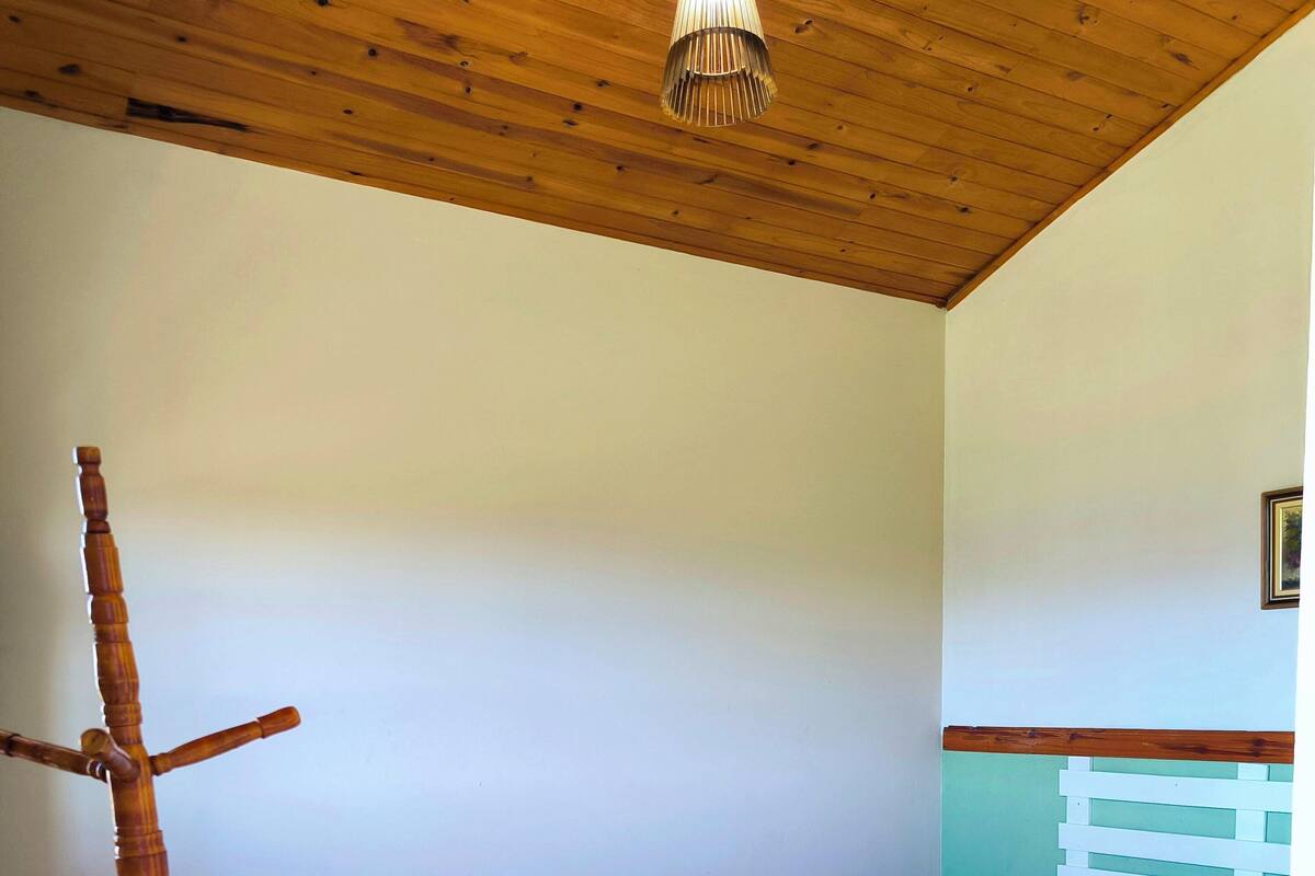 Un dormitorio con techo de madera, una cama con colcha estampada, una silla de madera y una mesita de noche con lámpara.