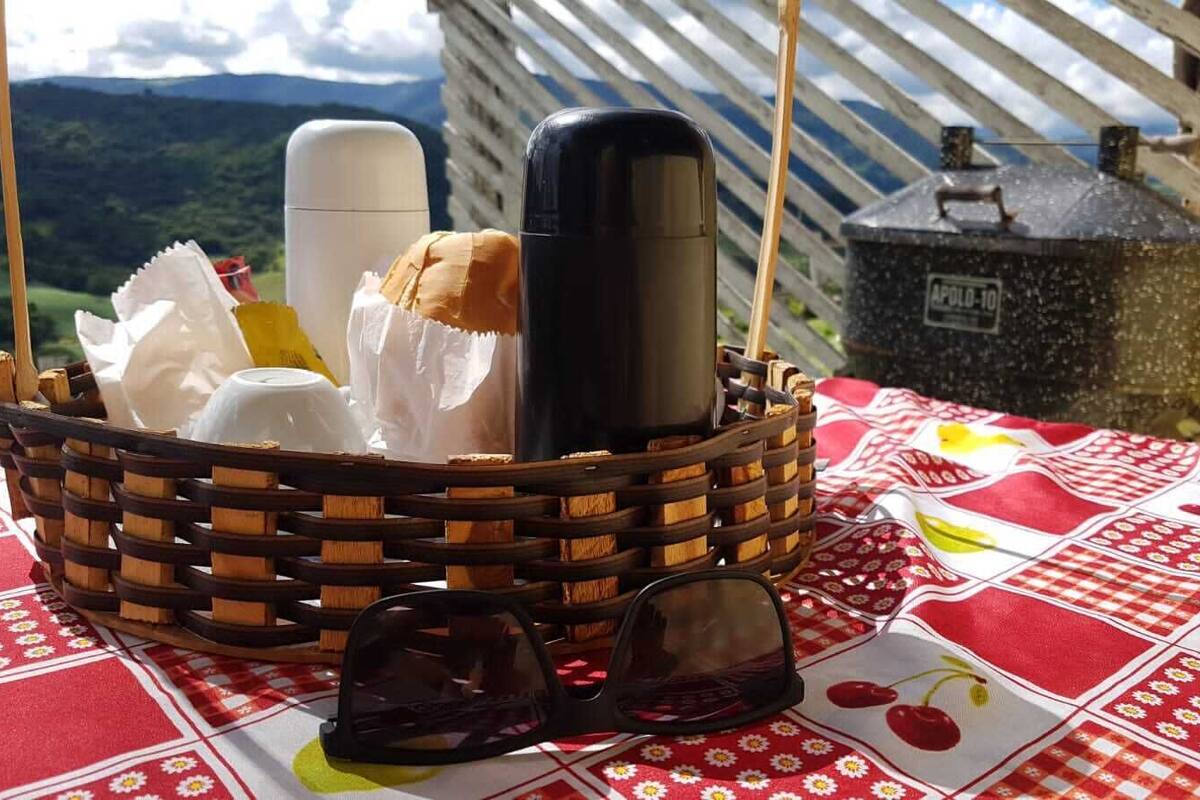 Una cesta de mimbre con alimentos y un objeto negro sobre un mantel a cuadros rojo y blanco.