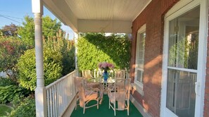 Eine überdachte Veranda mit Tisch und Stühlen, umgeben von Grünpflanzen.