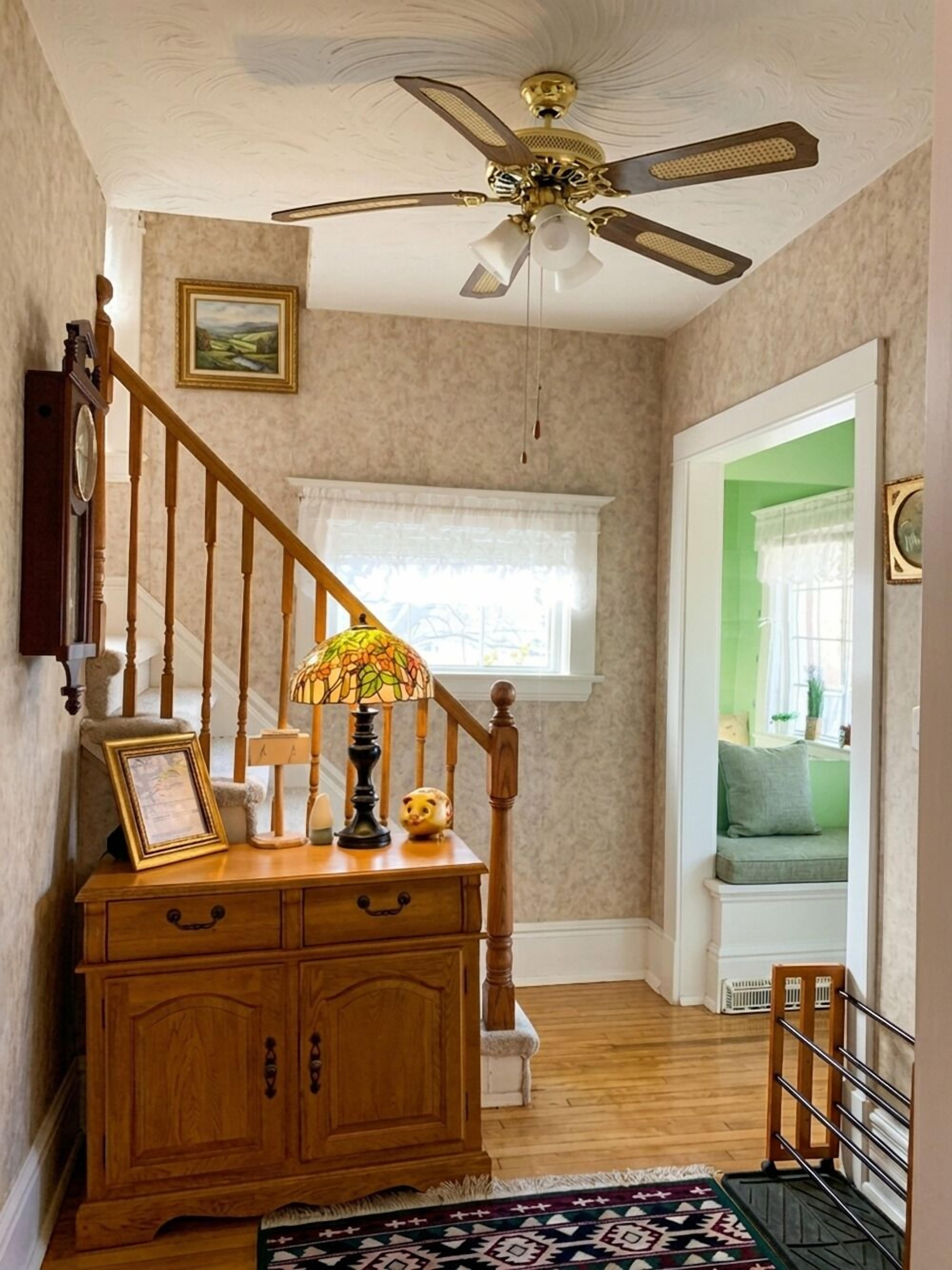 A staircase with a wooden handrail, a chandelier, and a wall-mounted clock.