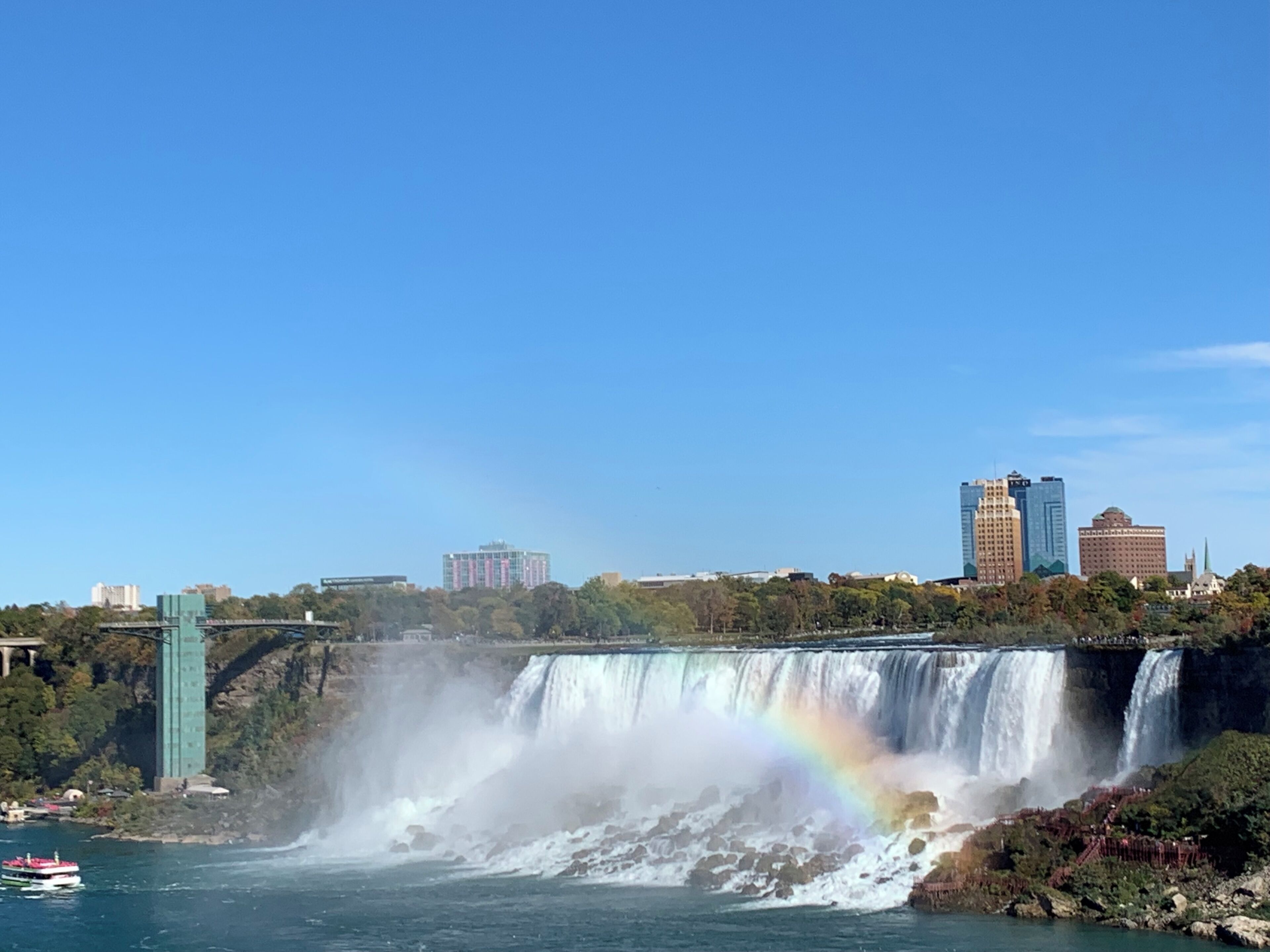 A waterfall with a rainbow, a bridge, and a cityscape in the background.