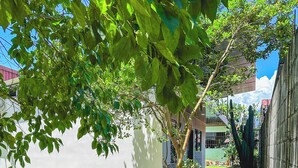 An outdoor patio with a round table and benches, surrounded by gravel, trees, and a cactus. - Cozy 2-bedroom apartment in charming La Fortuna with WiFi, AC (La Fortuna)