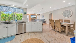 Een moderne keuken met witte kastjes, een groot eiland en een eethoek met rieten stoelen.