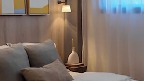 Una cama bien hecha con un edredón de color claro, una lámpara de noche y dos cuadros en la pared.