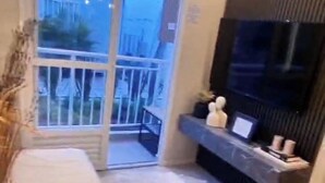 Una sala de estar moderna con un ventanal grande, un sofá blanco, una mesita con objetos decorativos y una pared de acento oscura.