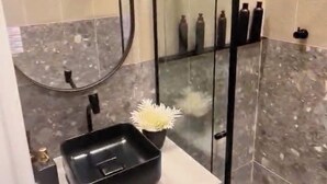 Un baño moderno con cabina de ducha de vidrio, lavamanos negro y espejo.