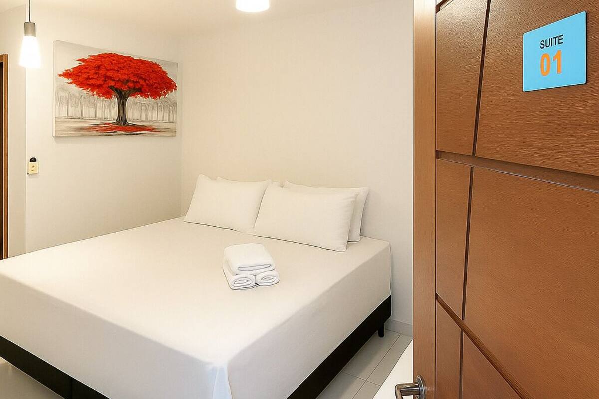 A hotel room with a bed, a painting of a tree, a sign indicating 'SUITE 01', and a wooden wardrobe.