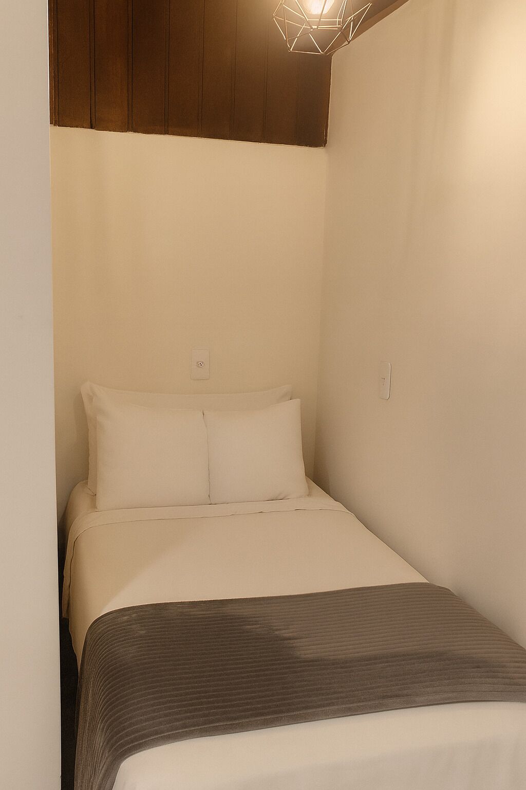 A single bed with a headboard, a bedside table, and a wall-mounted light fixture.