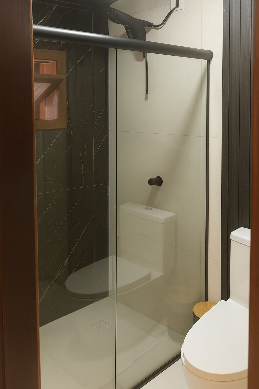 A glass-enclosed shower stall with a toilet and a towel rack.